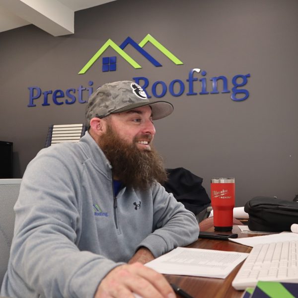 Prestige Roofing team member with a beard and camouflage hat works at an office desk